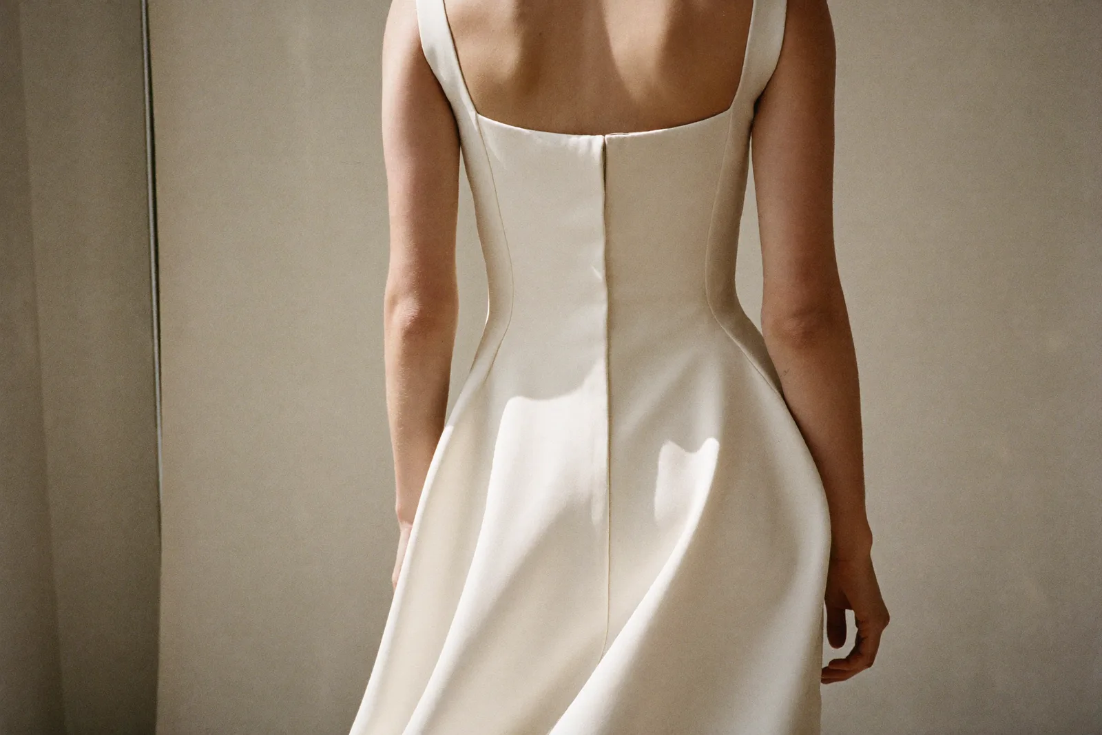 Braut in einem reduzierten, fließenden Brautkleid im weichen Tageslicht, klare Linien, feiner Stoff im Vordergrund